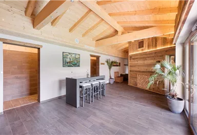 A modern, bright living space with a wooden ceiling and large windows. The room is decorated with a dining table and plants.