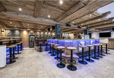 Eine moderne Bar mit Holzdekor und stimmungsvollem Licht. Die Sitzplätze sind um die zentrale Theke angeordnet.