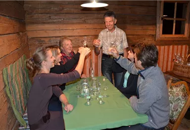 A group of five people is sitting at a table in a cozy wooden cabin. They are clinking glasses and celebrating together.