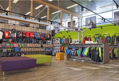 Ein moderner Outdoor-Laden mit bunten Rucksäcken und Jacken. Die Wände sind hellgrün und die Einrichtung ist ansprechend und funktional.