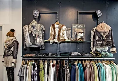 Ein moderner Modegeschäft mit stilvollen Bekleidungsstücken. An der Wand hängen verschiedene Jacken und Accessoires, während darunter eine Reihe von bunten Oberteilen präsentiert wird.