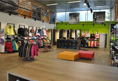 Ein moderner Sportbekleidungsstore mit bunten Jacken und Ausrüstung. In der Mitte stehen orangefarbene Sitze und die Wände sind mit Bildern dekoriert.