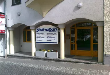 An entrance area of a building with a large advertising board for a travel company. The facade is brightly painted and has large windows.