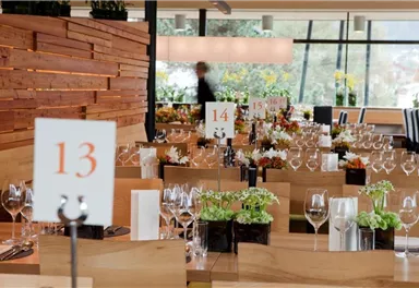 An elegant restaurant with beautifully decorated tables and flower arrangements. The tables are set with glasses and numbered signs.