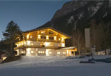 A charming, illuminated chalet in a snow-covered landscape. In the background, a majestic mountain rises.