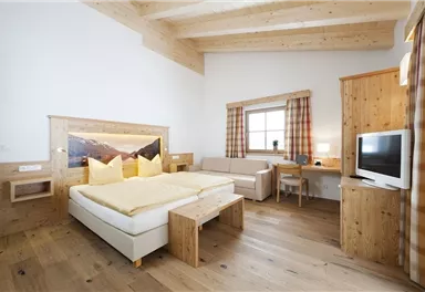 A modern hotel room with wooden furniture and a large double bed. The room has a bright atmosphere and is equipped with a desk and a television.