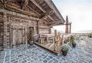 A rustic alpine cabin named "Rübezahl-Alm". The entrance area is adorned with flowers and wooden decorations.