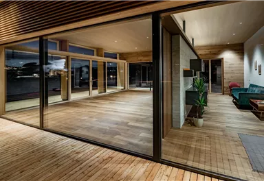 A modern residential building with large windows and wooden flooring. The room is bright and inviting, with a view of the surroundings.
