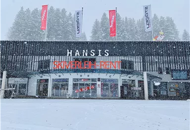 A ski rental named "Hansis" in the snow. The facade is modern, surrounded by snow-covered trees.