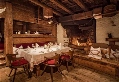 Ein gemütliches Restaurant mit einem Holzofen und rustikaler Einrichtung. Der Tisch ist für Gäste gedeckt und die Atmosphäre ist warm und einladend.