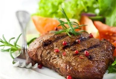 Juicy steak with red peppercorns, served with fresh salad and vegetables. A delicious dish on a white plate.