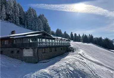 A picturesque mountain cabin in the snow, surrounded by snow-covered trees. The sky is clear and the sun is shining.