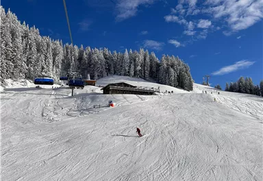 A snow-covered landscape with a ski lodge and lifts. Clear blue skies and snow-covered trees in the background.