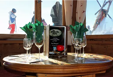 A cozy table in a mountain cabin with glasses and decorations. In the background, skiers can be seen.