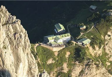 A secluded cabin in the mountains, surrounded by steep rocks and green terrain. The roofs are green and the landscape is lush and unspoiled.