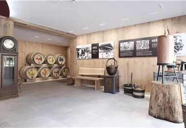 A room with wooden walls and floor, where historical barrels stand against a wall. There are seating areas and exhibits related to history.