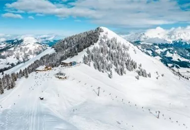 Eine schneebedeckte Berglandschaft mit einem Skigebiet. Im Hintergrund sind hohe Berge und ein klarer blauer Himmel zu sehen.