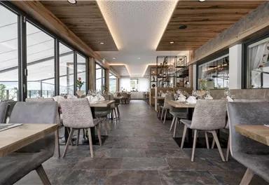 Ein modernes Restaurant mit hellem Ambiente und großen Fenstern. Holz- und Steinelemente schaffen eine einladende Atmosphäre.