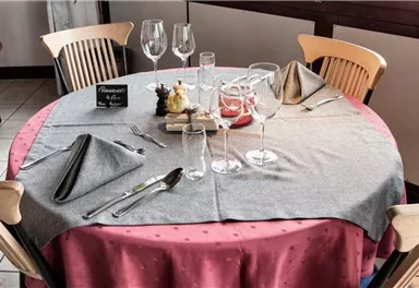 Ein schön gedeckter Tisch in einem Restaurant mit Glaswaren und eleganter Tischdekoration. Die Tischdecke ist grau mit roten Akzenten.