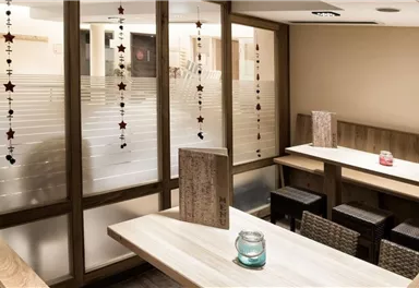 Ein gemütlicher Innenraum mit Holzmöbeln und einem modernen Design. Ein paar dekorative Elemente hängen von der Decke, und ein Tisch ist mit einer Kerze geschmückt.