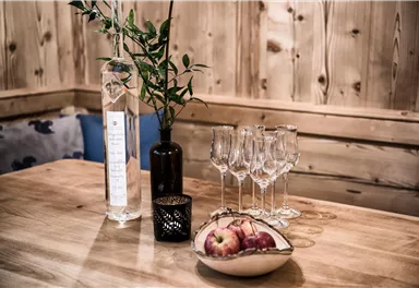 A table with an elegant arrangement of a bottle, glasses, and a fruit bowl with apples. The wooden paneling in the background creates a cozy atmosphere.
