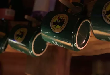 A series of green cups hang on a wooden shelf. Each cup has a logo on the front.
