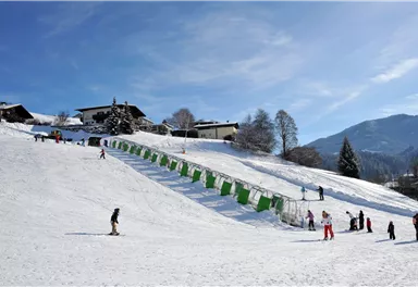 Ein verschneites Skigebiet mit einer Skilift-Anlage. Verschiedene Menschen genießen das Skifahren und Rodeln.