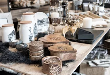 Ein stilvolles Arrangement aus Holzdekorationen, Kerzen und Geschirr auf einem Tisch. Verschiedene Accessoires und kunstvolle Objekte schaffen eine einladende Atmosphäre.