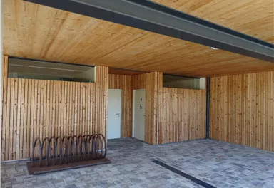 Ein moderner Raum mit Holzverkleidung und einer hellen Decke. Links befindet sich ein Fahrradständer und zwei Türen.