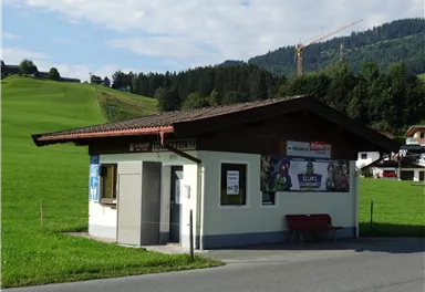 A small roadside stand, surrounded by green meadows. In the background, gentle hills and forests are visible.