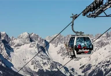 Eine Seilbahn fährt über schneebedeckte Berge. Der Himmel ist klar und blau, ideal für einen Skitag.