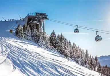 Eine Bergbahn in der winterlichen Landschaft mit schneebedeckten Pisten. Im Hintergrund sind verschneite Bäume und ein strahlend blauer Himmel zu sehen.