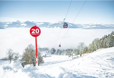 Eine malerische Winterlandschaft mit einem Skilift, der durch einen klaren Himmel fährt. Im Vordergrund steht ein Schild mit der Zahl 20.