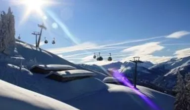 A snowy landscape with ski lifts and shining sun. The mountains and the sky are clear and blue.