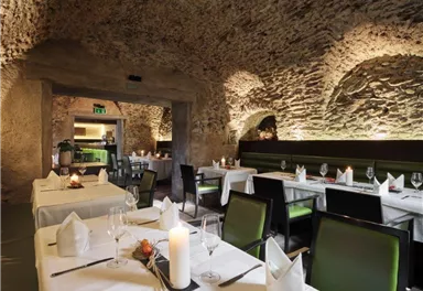 Ein elegantes Restaurant mit Steinmauern und weichem Licht. Die Tische sind festlich gedeckt und laden zum Verweilen ein.