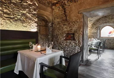 Ein gemütliches Restaurant mit steinernen Wänden und eleganten Tischen. Grüne Sitze und sanftes Licht schaffen eine einladende Atmosphäre.