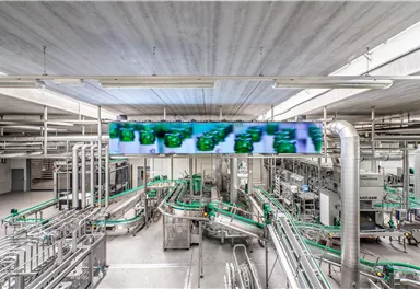 A modern production facility with many pipes and conveyor belts. In the background, a large screen can be seen displaying information.