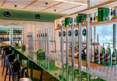 An elegant bar with green elements and a long counter. In the background, various drinks and glasses are visible.