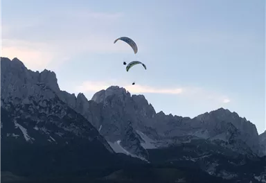 Zwei Gleitschirme fliegen über majestätische Berge. Der Himmel ist klar und zeigt die Schönheit der Natur.