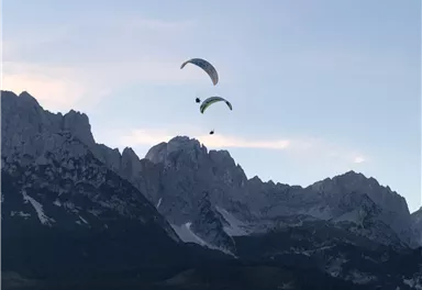 Zwei Gleitschirme fliegen über majestätische Berge. Der Himmel ist klar und zeigt die Schönheit der Natur.