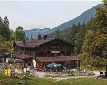 Ein traditionelles Gasthaus inmitten von Bäumen und Bergen. Der Außenbereich ist gemütlich und einladend.