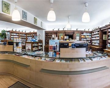 Eine helle Apotheke mit vielen Regalen voller Medikamente und einem modernen Empfangstresen. Die Wände sind dekoriert und die Atmosphäre wirkt einladend.