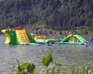 A colorful water attraction floats in the lake. Many people are having fun climbing and sliding.