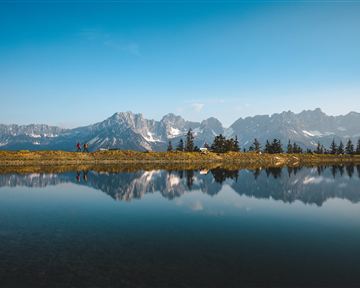 Eine malerische Berglandschaft mit schneebedeckten Gipfeln und einem ruhigen Wasser, das die Wolken spiegelt. Die Szenerie ist friedlich und einladend.