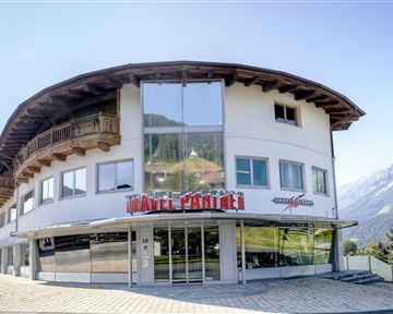 A modern building with large windows and a curved roof. In the background, there are mountains and a clear sky.