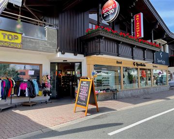 A sports store with a large selection of sports clothing and equipment. The facade is decorated with flowers, and there is a sign indicating special offers.