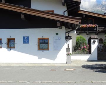 Ein traditionelles alpinisches Haus mit einem Parkplatzschild. Die Fassade ist in weißer Farbe gehalten und hat kleine Fenster mit Holzrahmen.