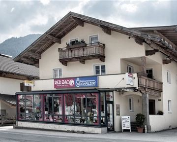 Ein traditionsches Gebäude in den Alpen mit einem gewerblichen Bereich im Erdgeschoss. Das Wetter ist bewölkt, schöne Bergkulisse im Hintergrund.