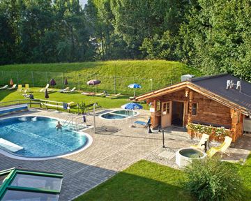 A beautiful outdoor area with a pool and hot tubs. In the background, there is a green meadow and a wooden hut.