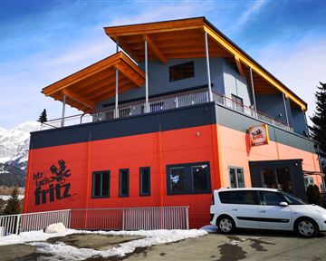 A modern building with an orange and gray design. It has a balcony and is located in a mountainous area.